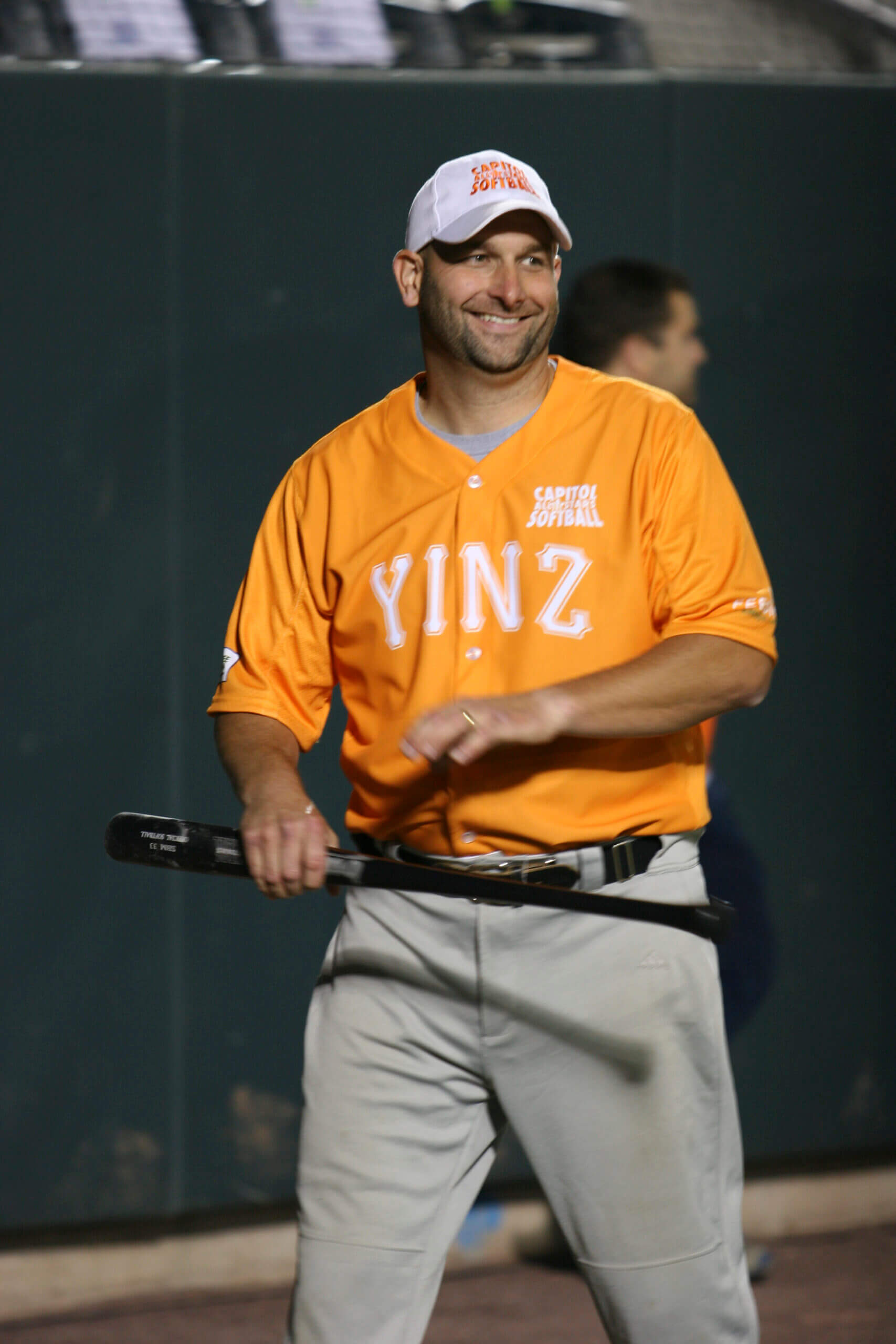 Mike Reese smiling in an orange Capitol All-Stars softball jersey, holding a bat