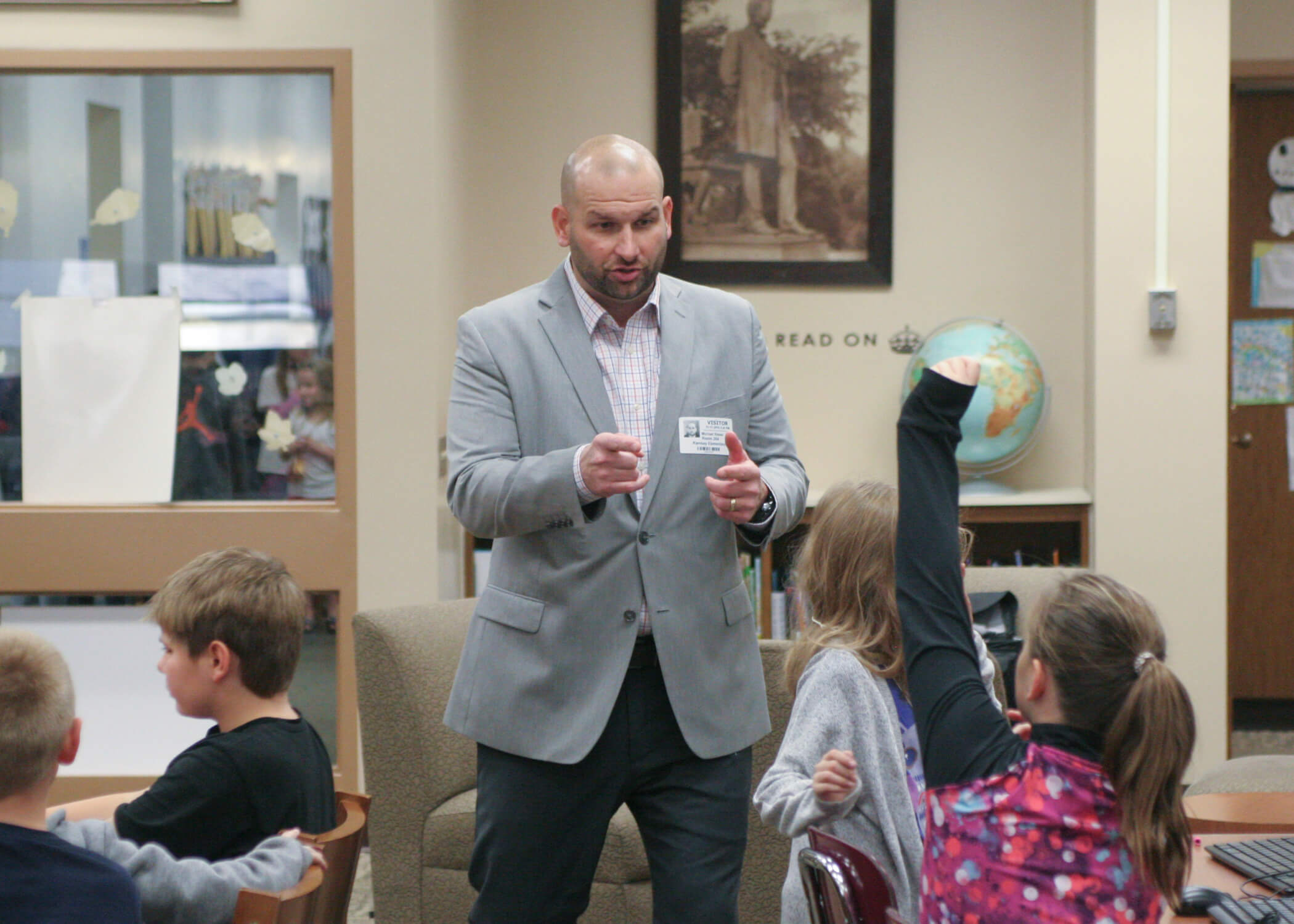 Mike Reese speaking with elementary school students in a school library, one child raising a hand
